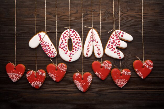 Parola &quot;amore&quot; fatta dei biscotti con i biscotti a forma di cuore appeso a corde su un tavolo di legno