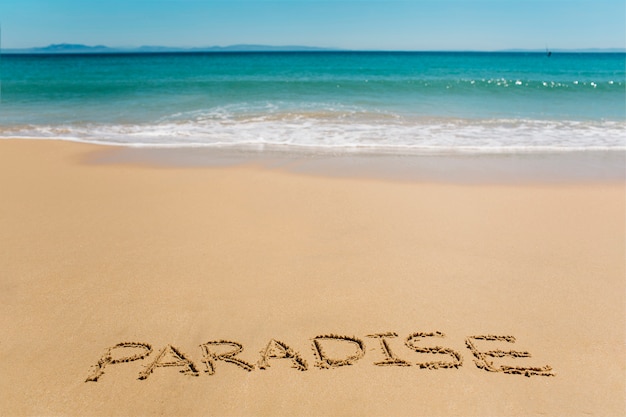 Parola di paradiso del fondo della spiaggia scritta in sabbia
