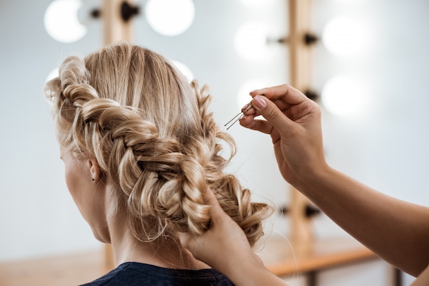 Parrucchiere femminile che fa acconciatura alla donna bionda nel salone di bellezza