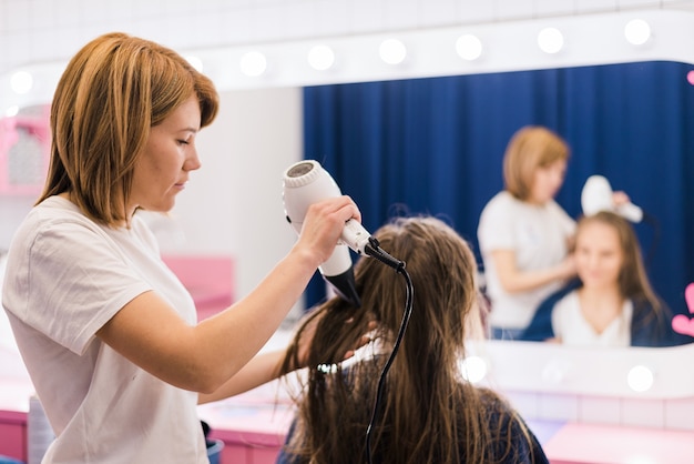 Parrucchiere femminile professionale che asciuga lo styling dei capelli della donna utilizzando asciugacapelli presso il salone di parrucchiere