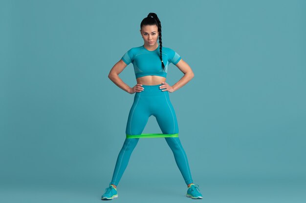 Parte inferiore del corpo. Bella giovane atleta femminile che pratica, ritratto blu monocromatico. Modello bruna dalla vestibilità sportiva con elastici. Body building, stile di vita sano, concetto di bellezza e azione.