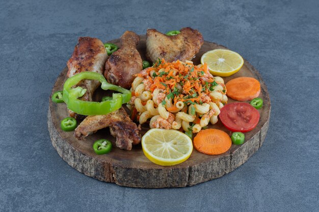 Parti di pollo arrosto e pasta su un pezzo di legno.