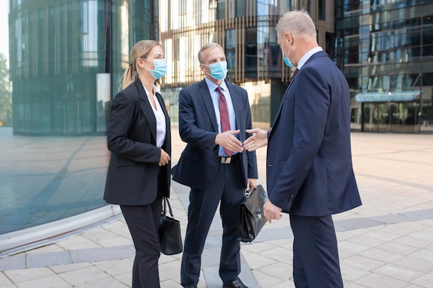 Partner commerciali di contenuti professionali in maschere facciali che si incontrano all'aperto e si salutano. Uomini d'affari fiduciosi che lavorano durante la pandemia di coronavirus. Il lavoro di squadra e il concetto di partnership