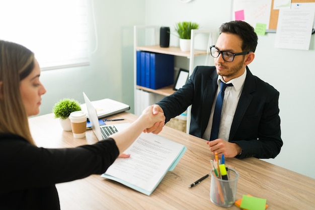 Partner d'affari in giacca e cravatta che stringe la mano a un collega professionista caucasico. Donna bionda che firma un accordo e un contratto con un avvocato in un ufficio aziendale