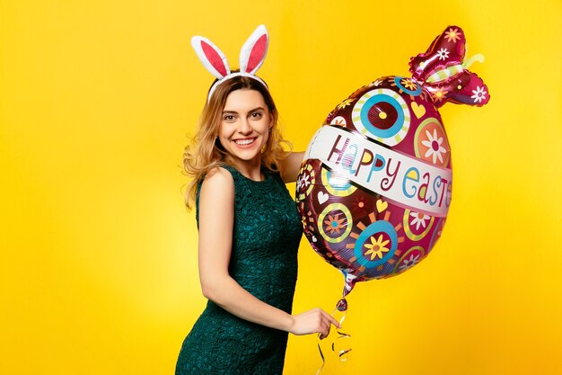 Pasqua. Felice ragazza sorridente in abito verde e orecchie da coniglio con palloncino a forma di uovo