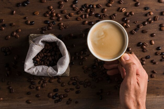 Passi la tazza della tenuta con caffè vicino al sacco con i fagioli