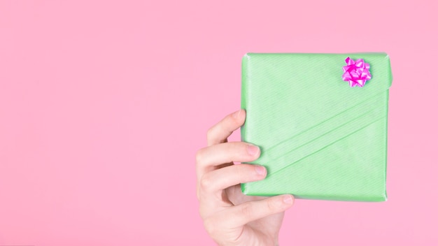 Passi la tenuta del contenitore di regalo avvolto verde con l&#39;arco rosa contro fondo colorato
