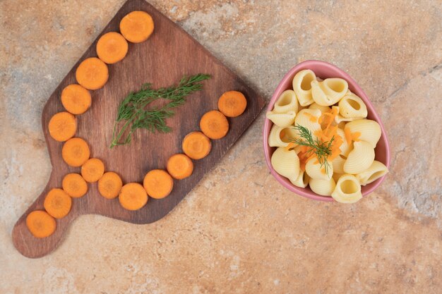 Pasta a forma di conchiglia con fette di carota e aneto in una ciotola