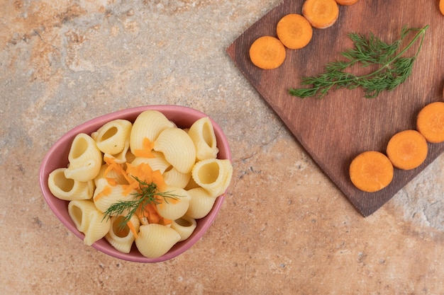 Pasta a forma di conchiglia con fette di carota e aneto in una ciotola.