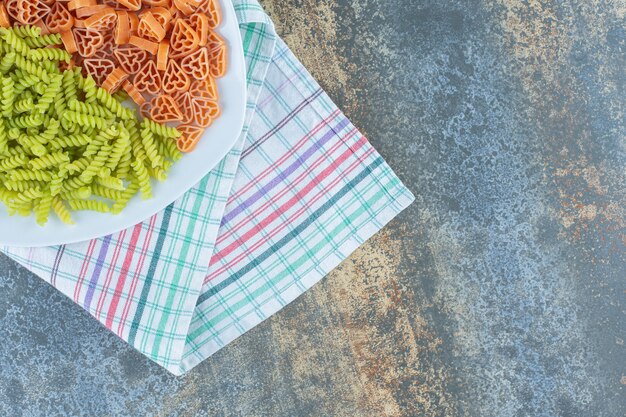 Pasta a forma di cuore con fusilli nel piatto, sul canovaccio, sulla superficie di marmo.