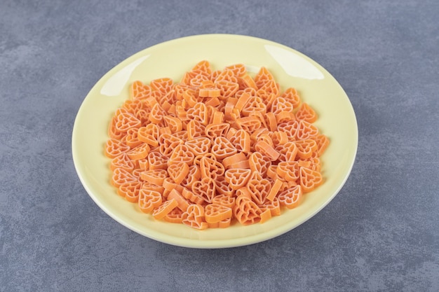 Pasta a forma di cuore cruda sul piatto giallo.