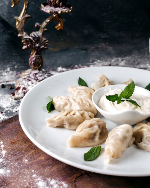 Pasta affettata con carne all'interno di foglie tritate e verdi all'interno del piatto bianco sulla superficie della luce