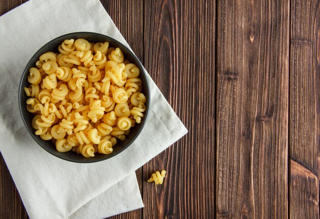 Pasta asciutta in una ciotola sul fondo dell'asciugamano di cucina e di legno. disteso.