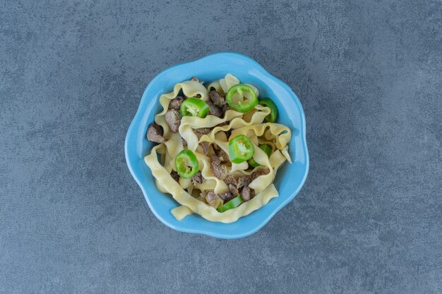 Pasta bollita con parti di carne in una ciotola blu.