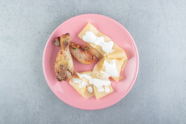 Pasta con yogurt e coscia di pollo sul piatto rosa.