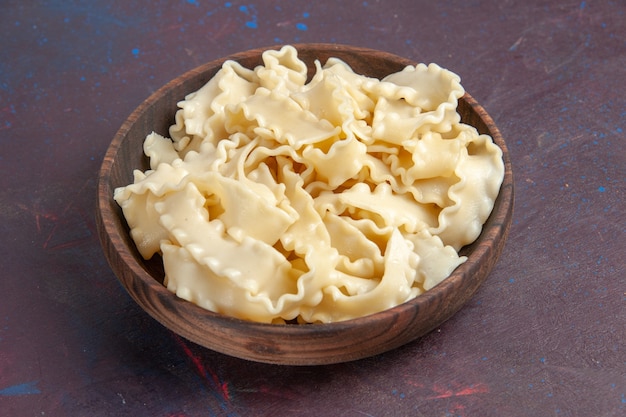 Pasta cruda affettata vista frontale all'interno del piatto marrone su uno spazio scuro