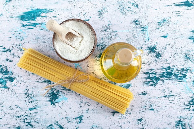 Pasta cruda degli spaghetti con la bottiglia dell'olio e della farina su fondo bianco. Foto di alta qualità