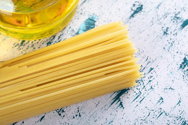 Pasta cruda degli spaghetti con la bottiglia di olio su bianco.