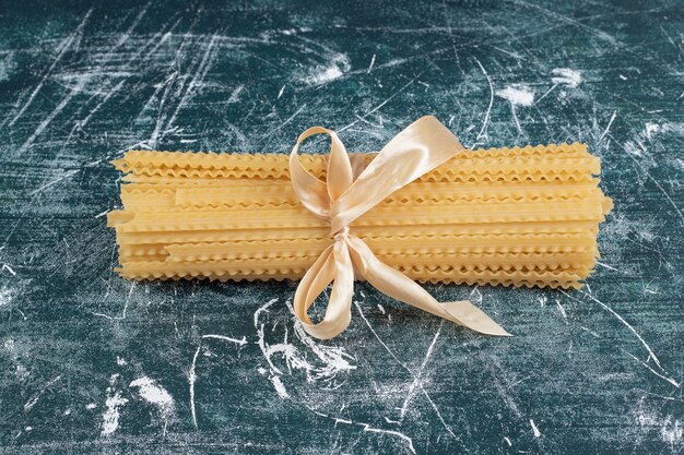 Pasta cruda delle mafaldine legata con il nastro sulla tavola blu. Foto di alta qualità