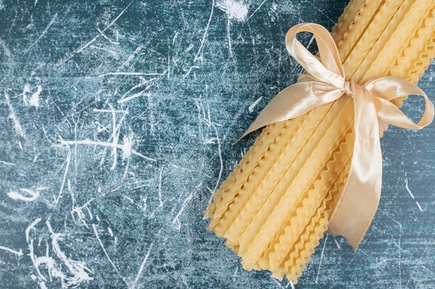 Pasta cruda delle mafaldine legata con il nastro sulla tavola blu. Foto di alta qualità