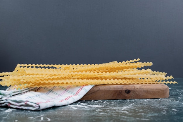 Pasta cruda gialla con tovaglia su tavola di legno.