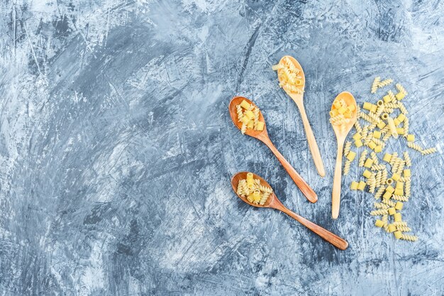 Pasta cruda in cucchiai di legno vista dall'alto su uno sfondo di intonaco grigio