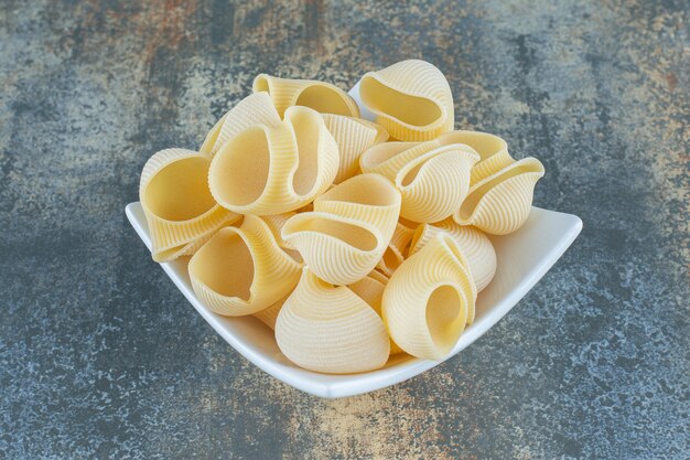 Pasta cruda nella ciotola, sulla superficie di marmo.