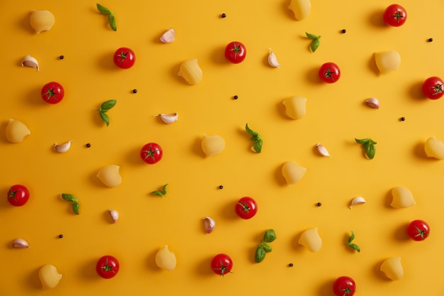 Pasta cruda, pomodori rossi, foglie di basilico e pepe in grani su sfondo giallo. Ingredienti per preparare deliziose paste. Cucina o cucina tradizionale italiana. Prodotti per la cucina. Vista dall'alto