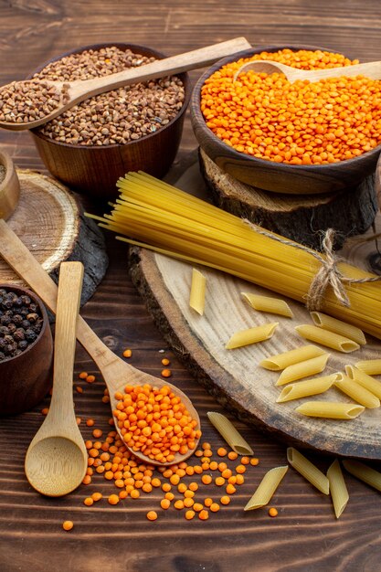 Pasta cruda vista frontale con grano saraceno e lenticchie su superficie marrone