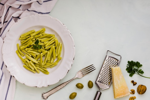 Pasta dei gemelli degli spinaci sul piatto ceramico bianco con gli ingredienti sul contesto bianco