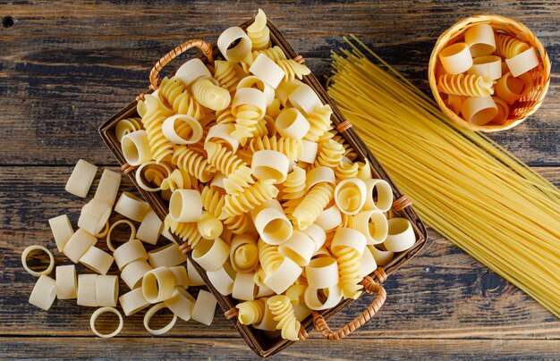 Pasta dei maccheroni di vista superiore in vassoio e piccolo secchio con gli spaghetti su fondo di legno. orizzontale