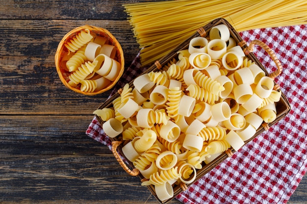 Pasta dei maccheroni in un canestro e secchio con la vista superiore degli spaghetti su un panno di picnic e su un fondo di legno