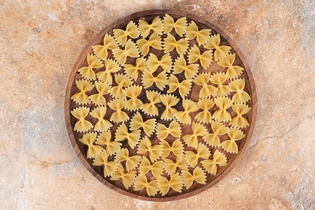 Pasta del farfallino sul piatto di legno su fondo di marmo. Foto di alta qualità