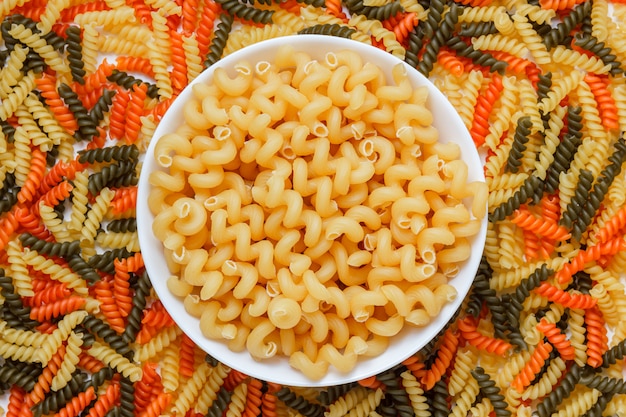 Pasta di Cellentani in un piatto bianco su un fusilli colorato sulla tavola bianca. disteso.