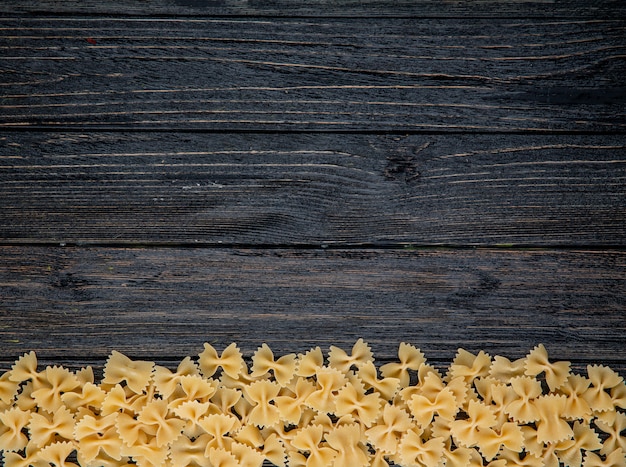 Pasta di farfalle vista dall'alto sul fondo con copia spazio su fondo di legno nero