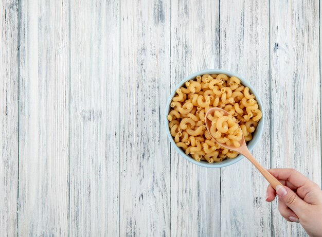 Pasta di maccheroni del gomito di vista superiore in ciotola a destra con lo spazio della copia su fondo di legno bianco