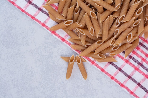 Pasta di penne marrone cruda sulla tovaglia a strisce