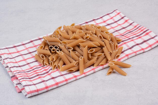 Pasta di penne marrone cruda sulla tovaglia a strisce.