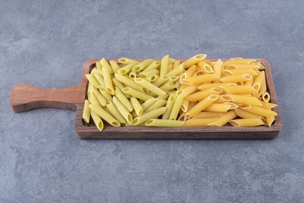 Pasta di penne verde e gialla cruda sul bordo di legno.