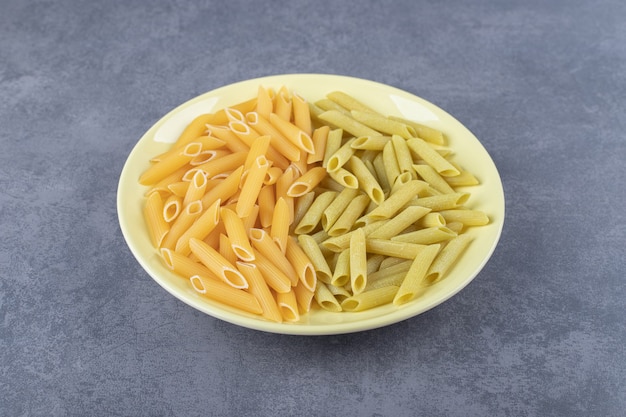 Pasta di penne verde e gialla cruda sul piatto giallo.