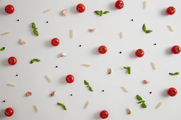 Pasta di riso crudo e ingredienti su sfondo bianco. Pomodori freschi, aglio, basilico da aggiungere alla cucina tradizionale italiana. Cercando la migliore ricetta. Piatto di maccheroni gourmet. Concetto di cucina. Cibo nutriente