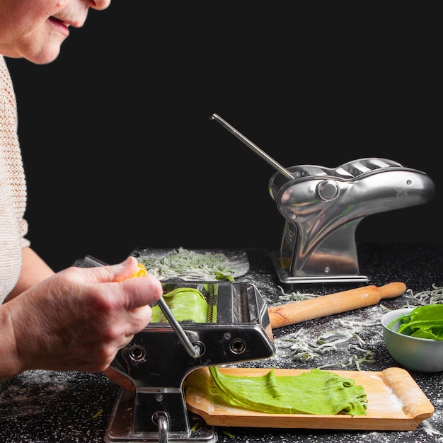 Pasta di taglio della donna di vista laterale in cucina con gli strumenti della cucina su fondo nero.