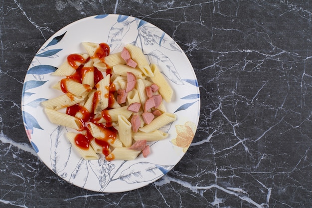 Pasta fresca di penne bollita con ketchup e salsiccia sulla ciotola bianca.