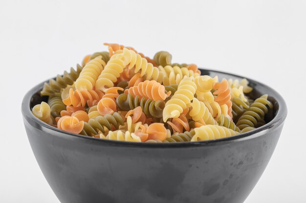 Pasta fusilli colorata cruda in ciotola scura. Foto di alta qualità