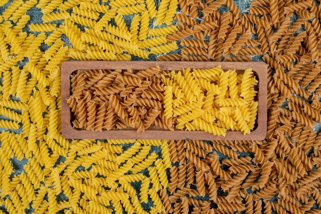 Pasta fusilli cruda gialla e marrone sul piatto di legno.