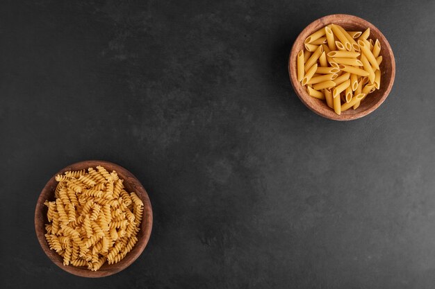 Pasta in coppe di legno opposte su sfondo nero.