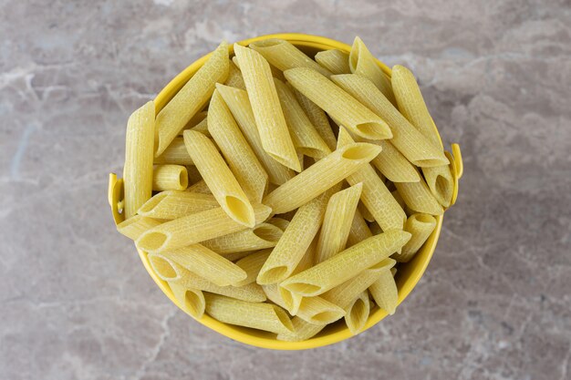 Pasta in secchio giallo, sulla superficie di marmo.