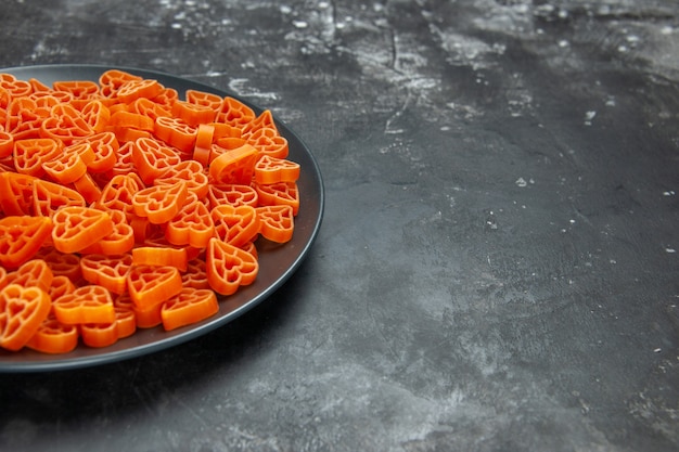 Pasta italiana a forma di cuore con vista a metà inferiore su piatto ovale nero su superficie scura