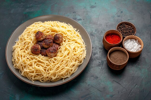 Pasta italiana cotta a metà vista con polpette e condimenti su superficie blu scuro