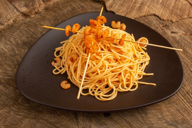 pasta italiana cotta con gamberetti all'interno del piatto marrone sulla scrivania in legno